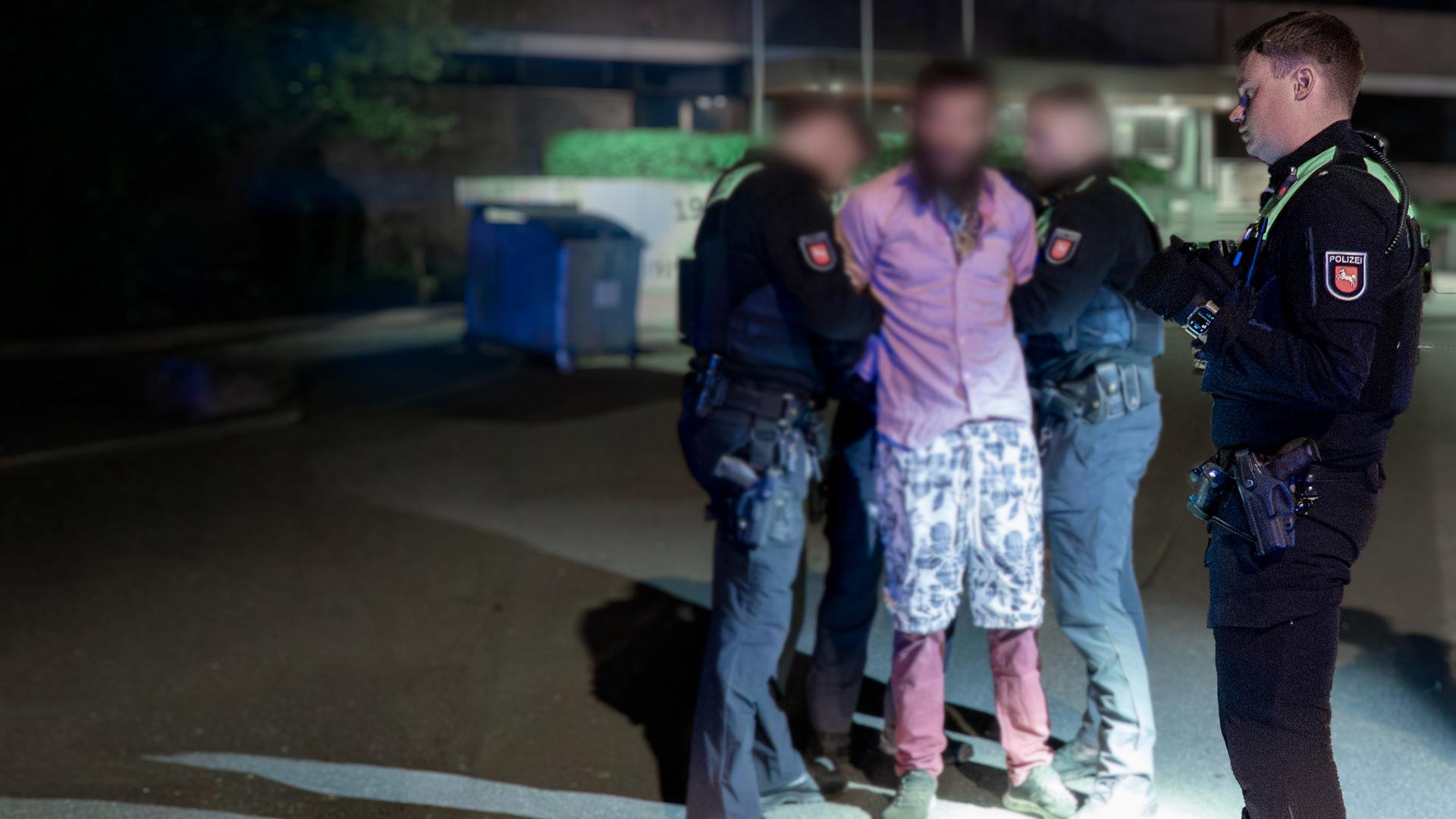 Ein unkenntlich gemachter Mann wird von zwei Polizisten festgehalten, daneben ein weiterer Polizist, der sich etwas notiert. 