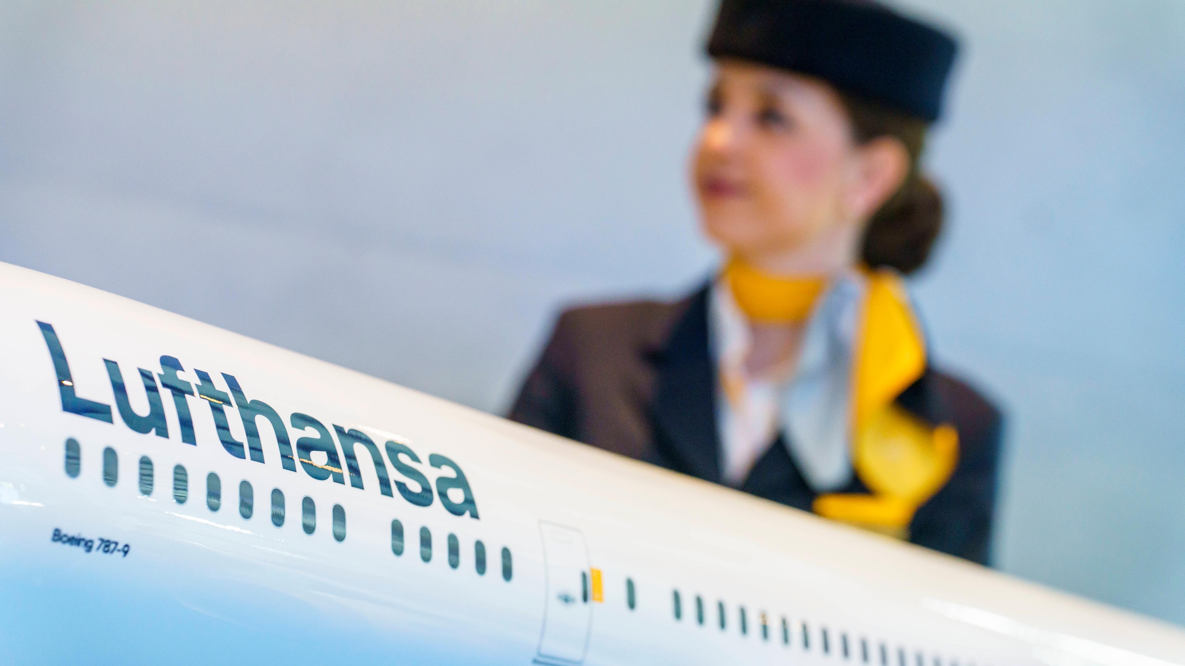 Eine Flugbegleiterin steht hinter einem Modell einer Lufthansamaschine.