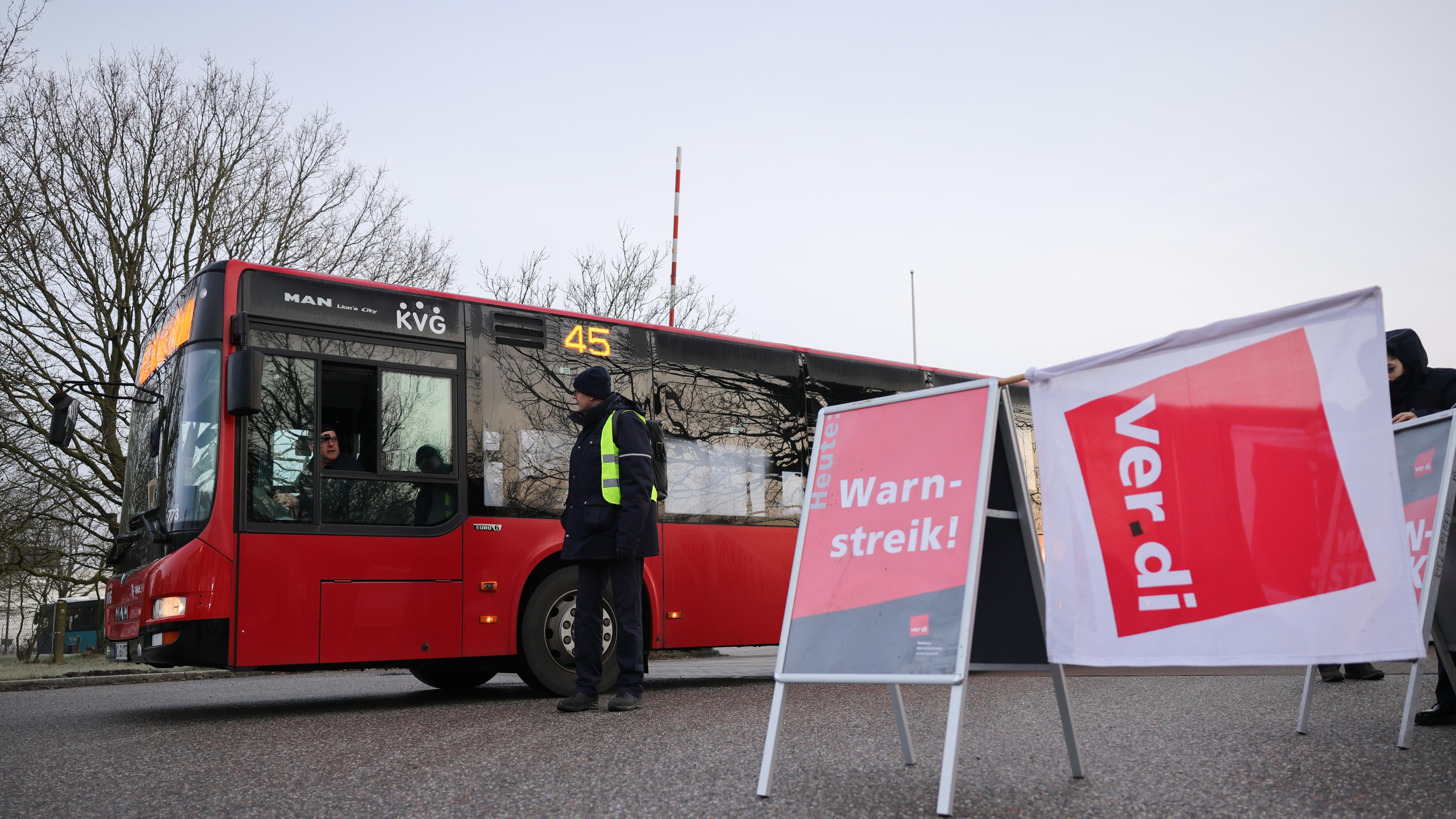 Archiv, 26.02.2024, Schleswig-Holstein, Kiel: Ein Schild mit der Aufschrift "Warnstreik" und eine Verdi-Flagge sind vor einem stehenden Bus zu sehen.