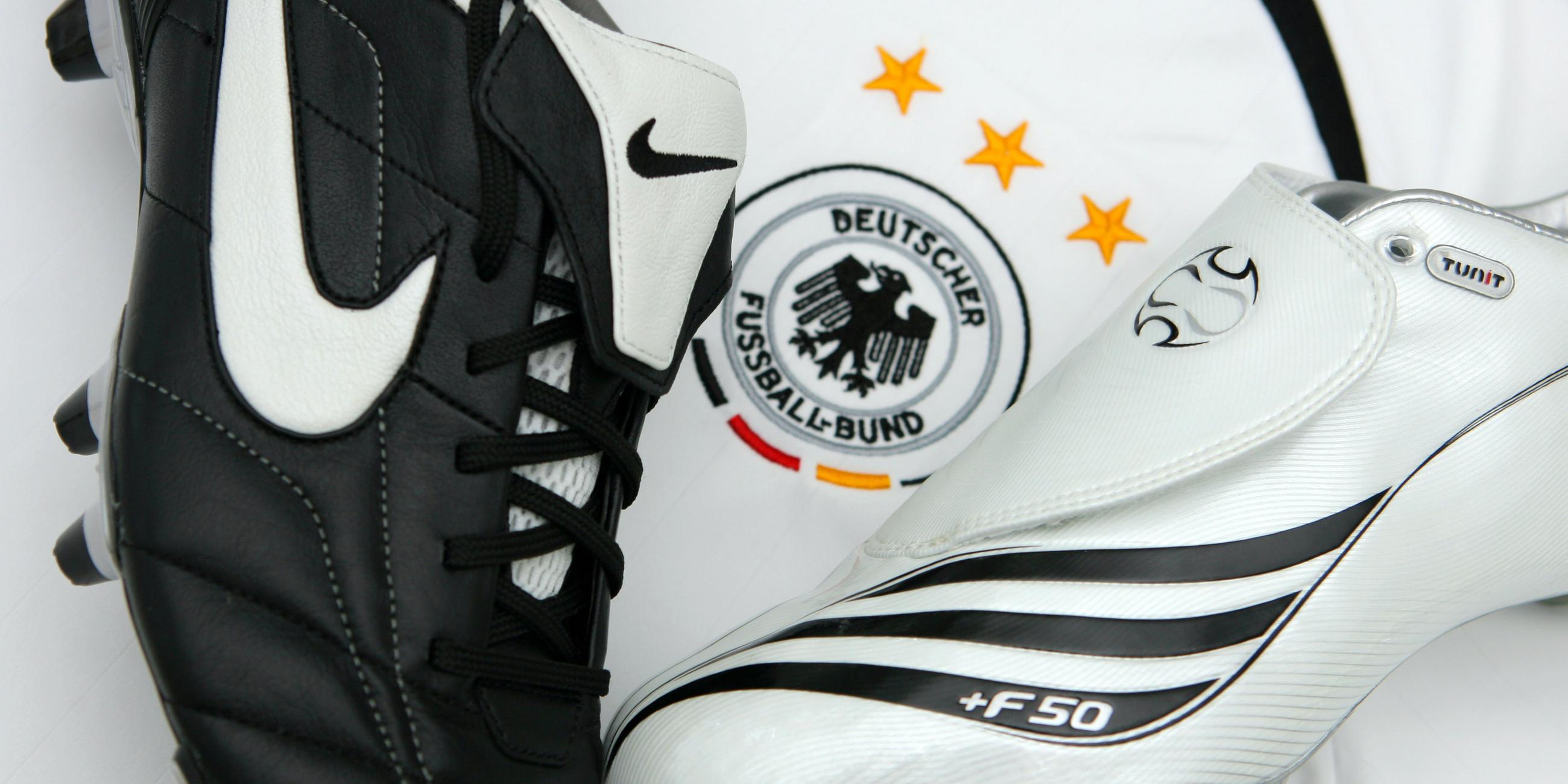 Fußballschuhe des Herzogenauracher Sportartikelherstellers Adidas (r) und der US-Firma Nike liegen auf einem Trikot der deutschen Fußball-Nationalmannschaft.