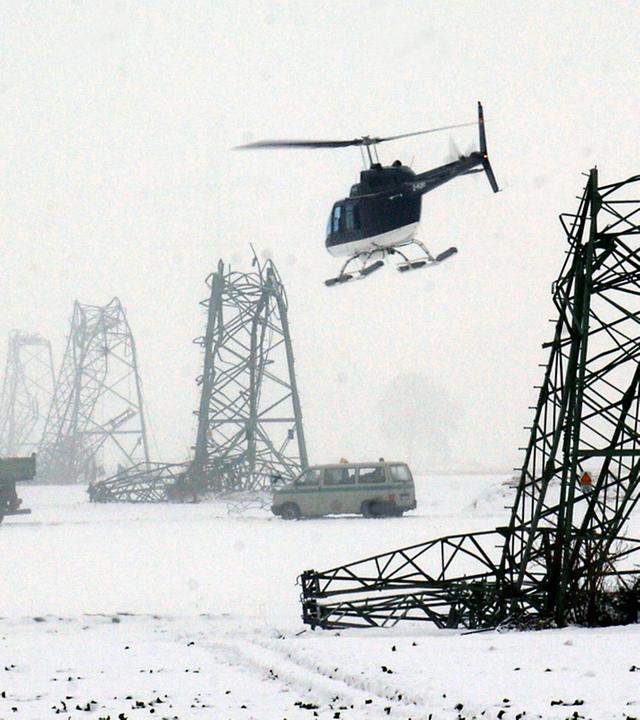 Umgeknickte Strommasten in verschneiter Landschaft