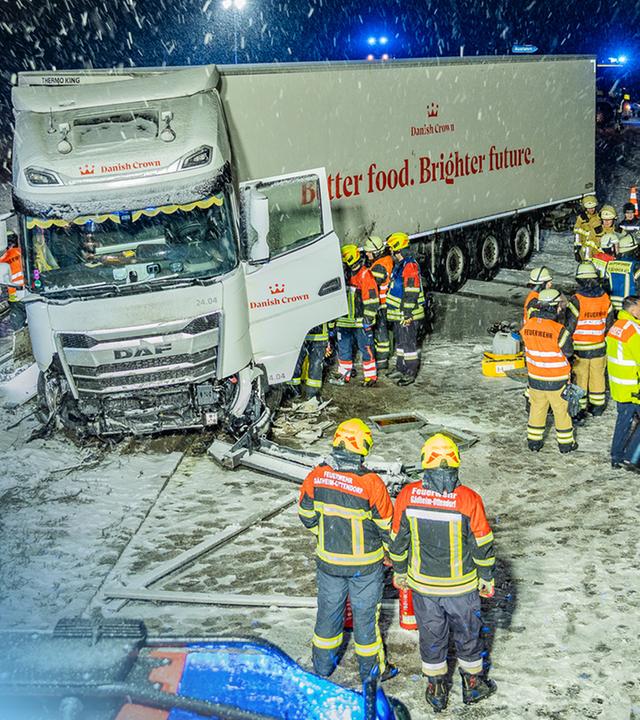 Ein demolierter LKW im Schnee auf einer Autobahn von Einsatzkräften umgeben