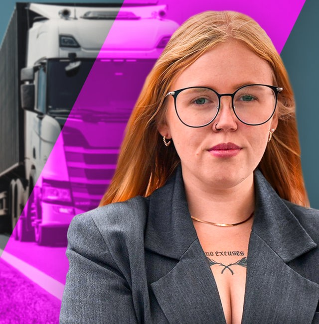 Eine junge Frau mit Brille verschränkt die Arme. Im Hintergrund fährt ein großer LKW auf einer Straße.