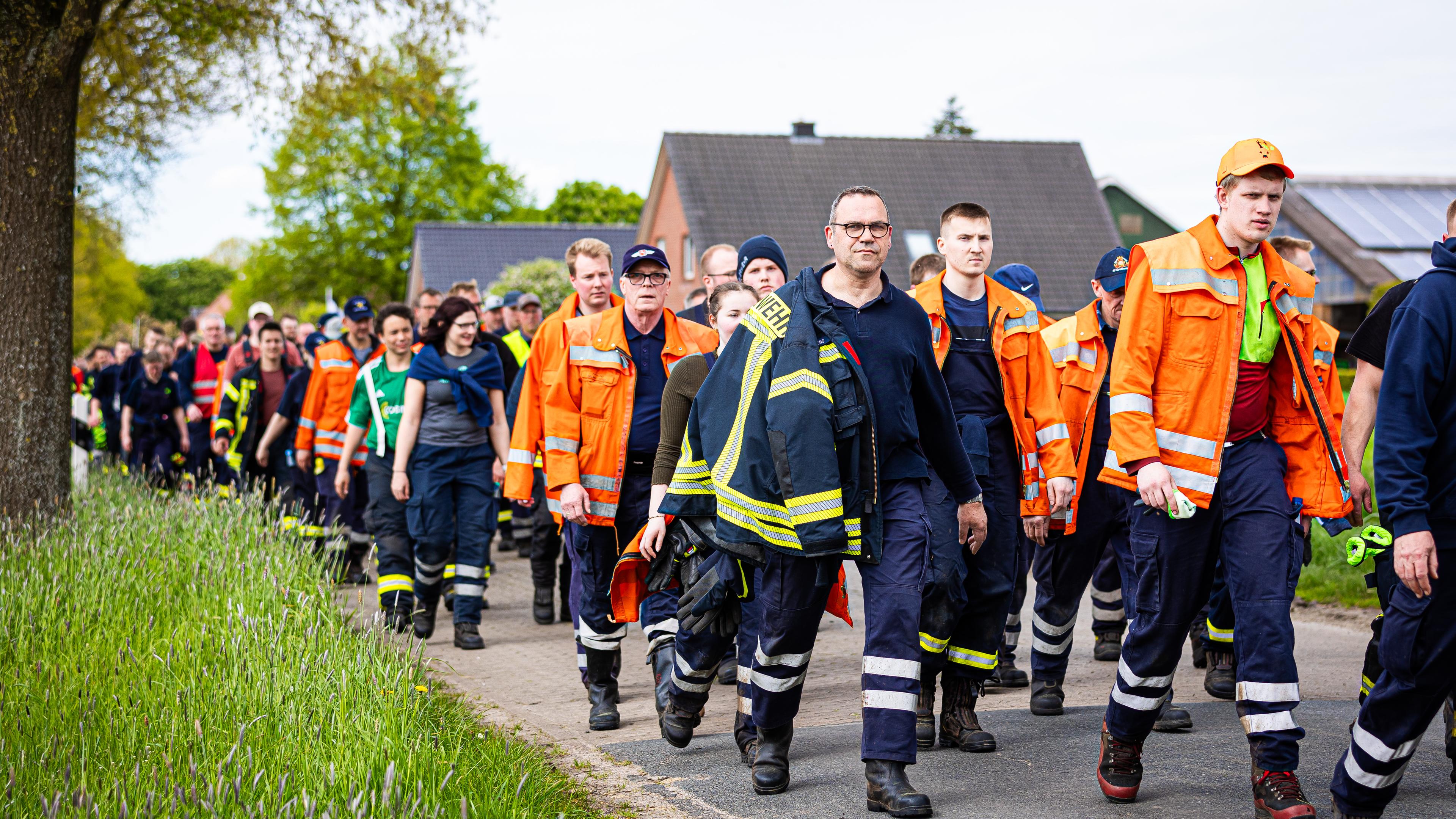Niedersachsen, Gräpel: Einsatzkräfte der Feuerwehr gehen eine Straße im Landkreis Stade entlang. 