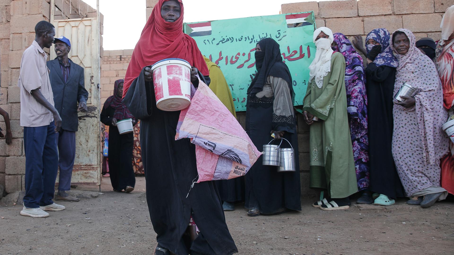 Verhüllte Frauen stehen mit Metallbehältern für Essen an.