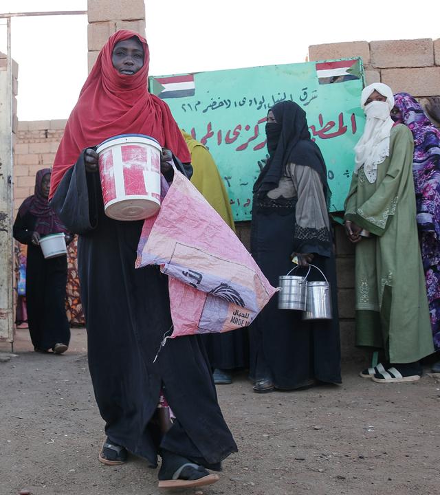 Verhüllte Frauen stehen mit Metallbehältern für Essen an.