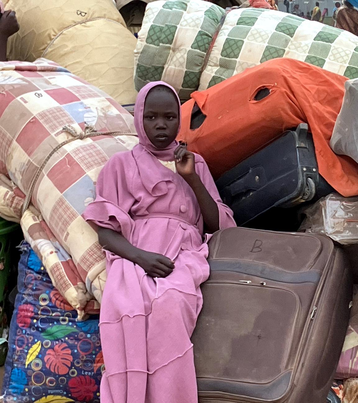 Eine junge Frau aus dem Sudan sitzt in einem Flüchtlingslager inmitten von Koffern
