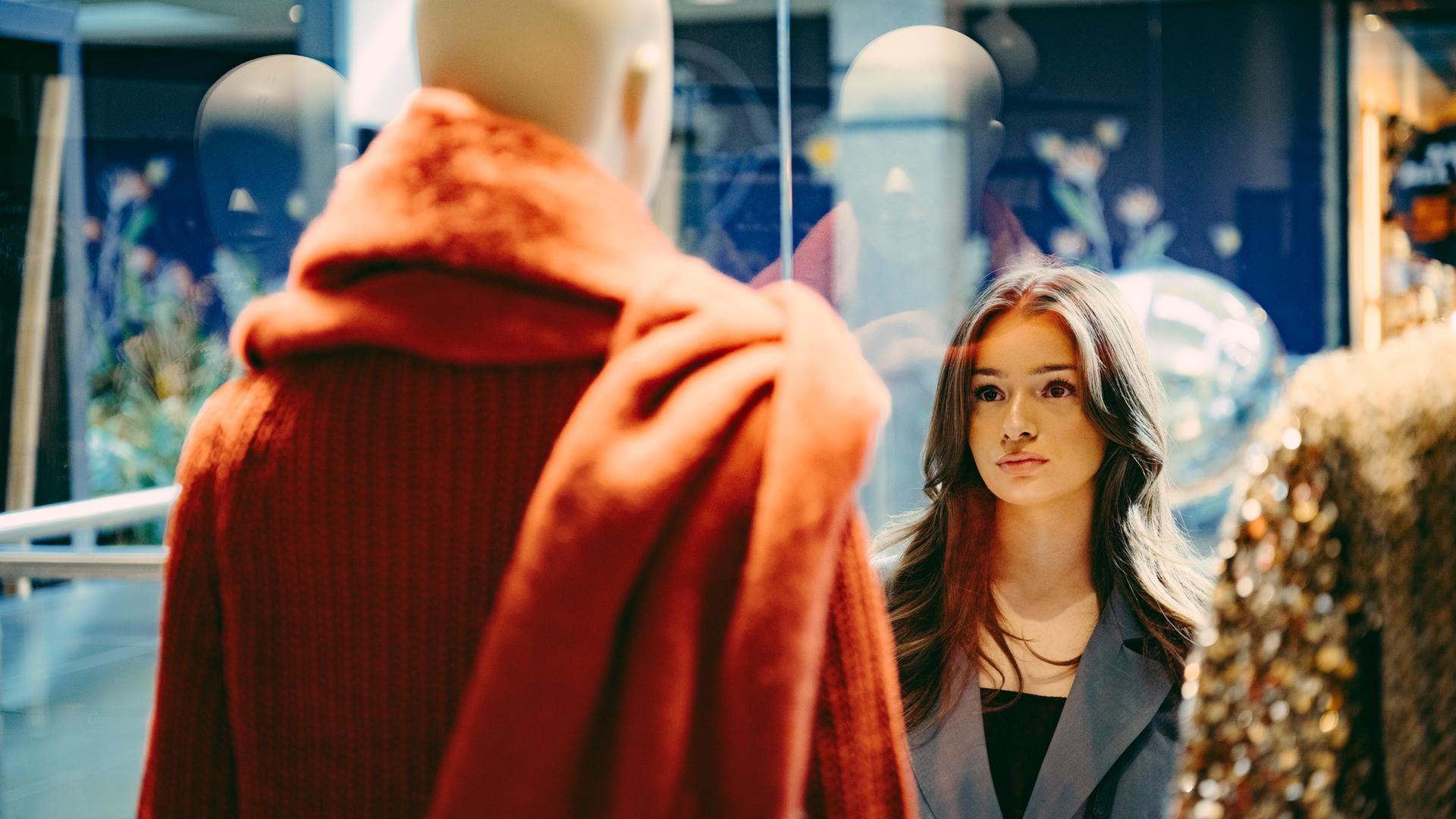 Sinem steht vor einem Schaufenster und schaut sich die Schaufensterpuppe an