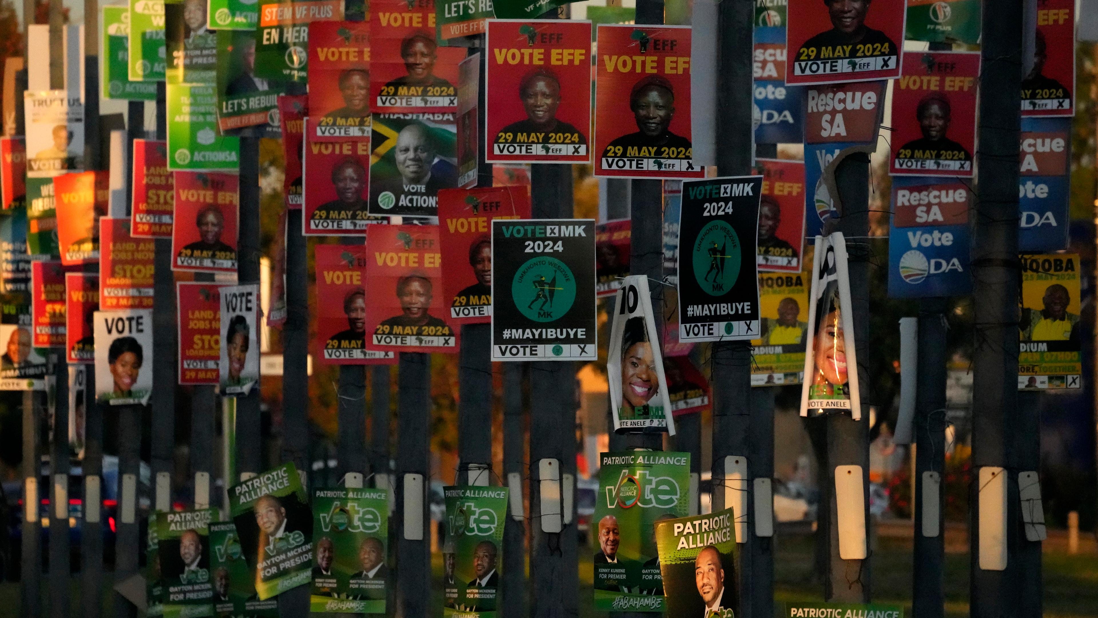Auf einer Straße in Südafrika sind eine große Menge an Wahlplakaten an Masten angebracht.