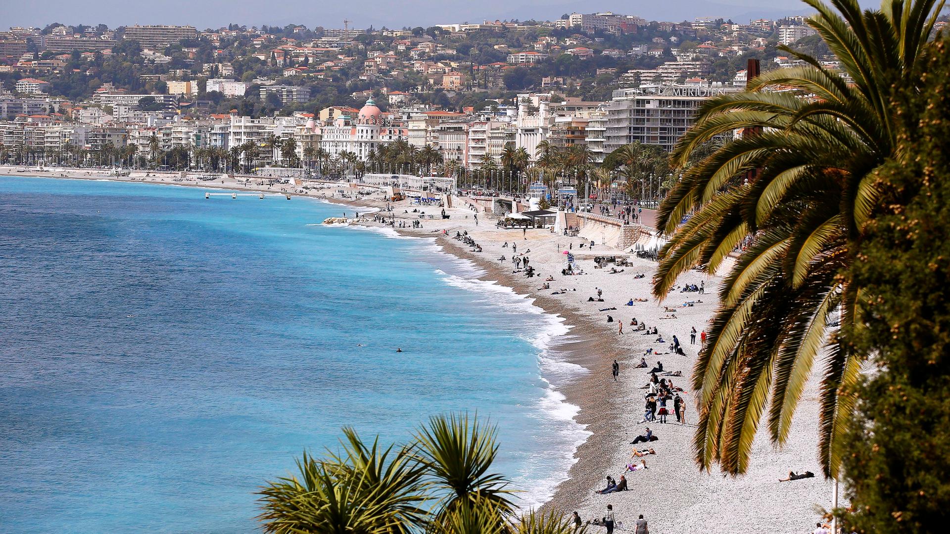 Ansicht der Promenade des Anglais in Nizza, mit Strand und Meer und vielen Häusern.