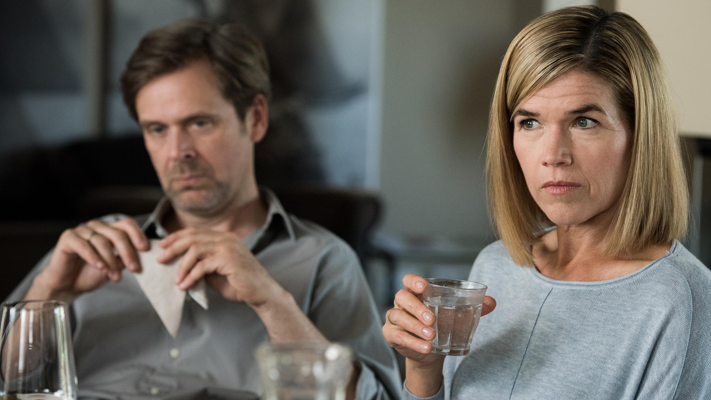"Südstadt": Martin Lehmann (Matthias Matschke) sitzt gelangweilt an einem Tisch und starrt ins Leere. Seine Frau Anne Lehmann (Anke Engelke) hält ein Glas Wasser in der Hand und schaut ernst nach vorne