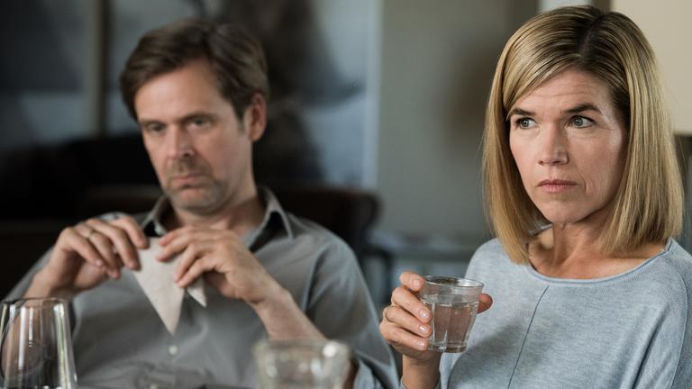 "Südstadt": Martin Lehmann (Matthias Matschke) sitzt gelangweilt an einem Tisch und starrt ins Leere. Seine Frau Anne Lehmann (Anke Engelke) hält ein Glas Wasser in der Hand und schaut ernst nach vorne