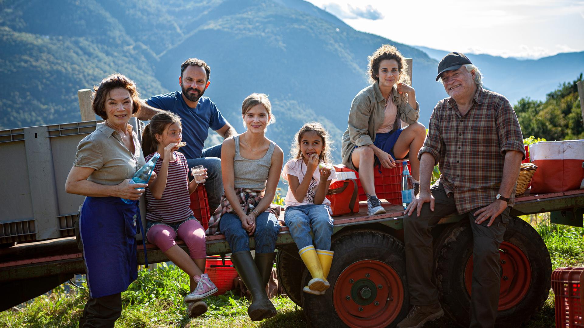 "Ein Sommer in Südtirol": Theresa Gasser (Julia Stemberger), Marco Antonelli (Sam Loris), Manfred Pichler (Emilio De Marchi) sind mit den Kindern von Marco und anderen Erntehelfern auf dem Anhänger eines Traktors zu sehen, wie sie gerade eine Pause machen und etwas trinken.