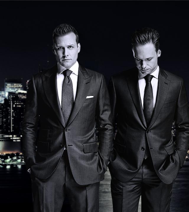 Star-Anwalt Harvey Specter und der clevere Mike Ross stehen nachts in teuren Anzügen vor der New Yorker Skyline.