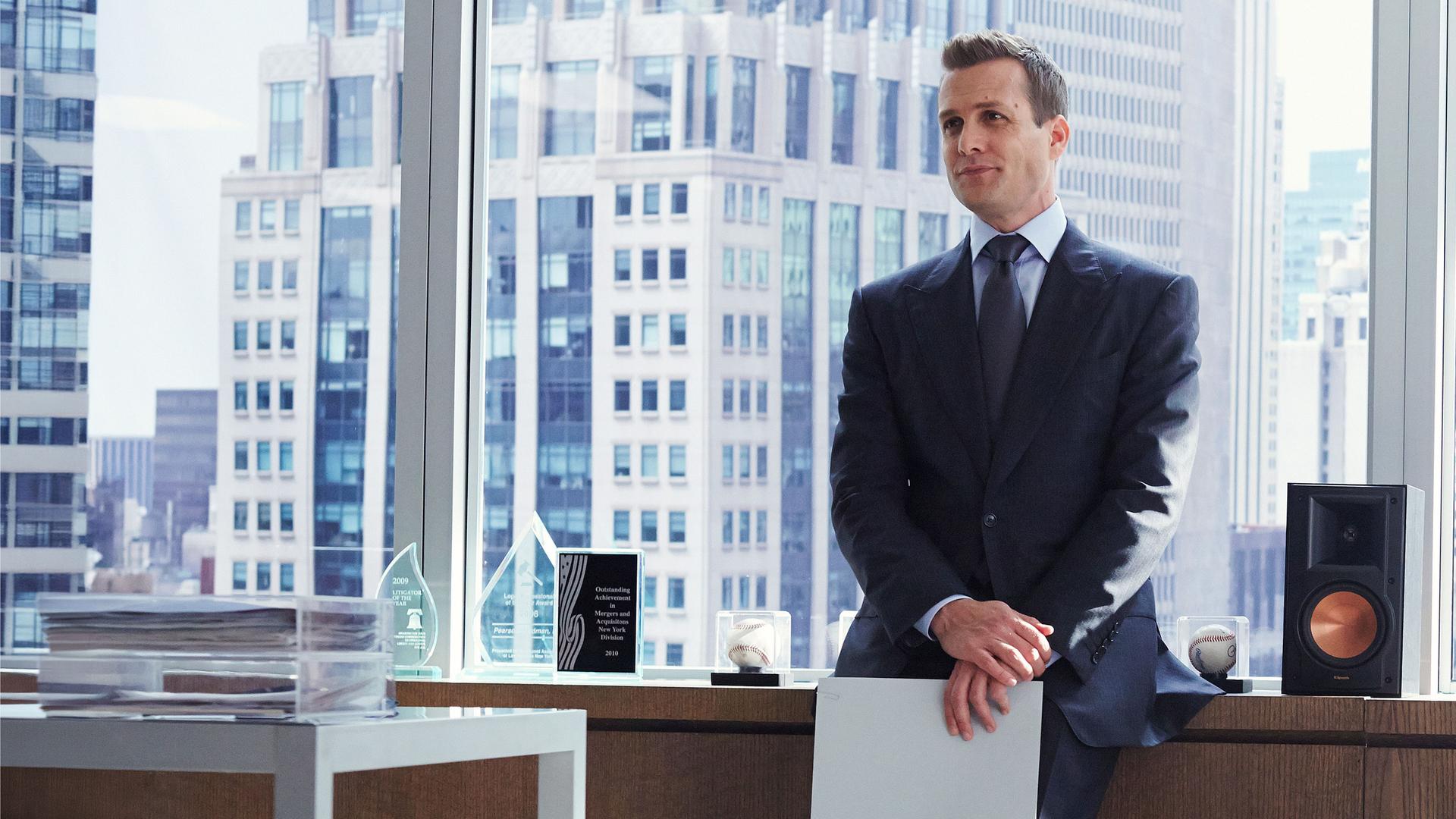 "Suits - Private Einsichten": Harvey (Gabriel Macht) steht im Anzug in einem Büro, lässig an ein Sideboard gelehnt. Hinter ihm sind große Fenster mit Blick auf die Skyline zu sehen.
