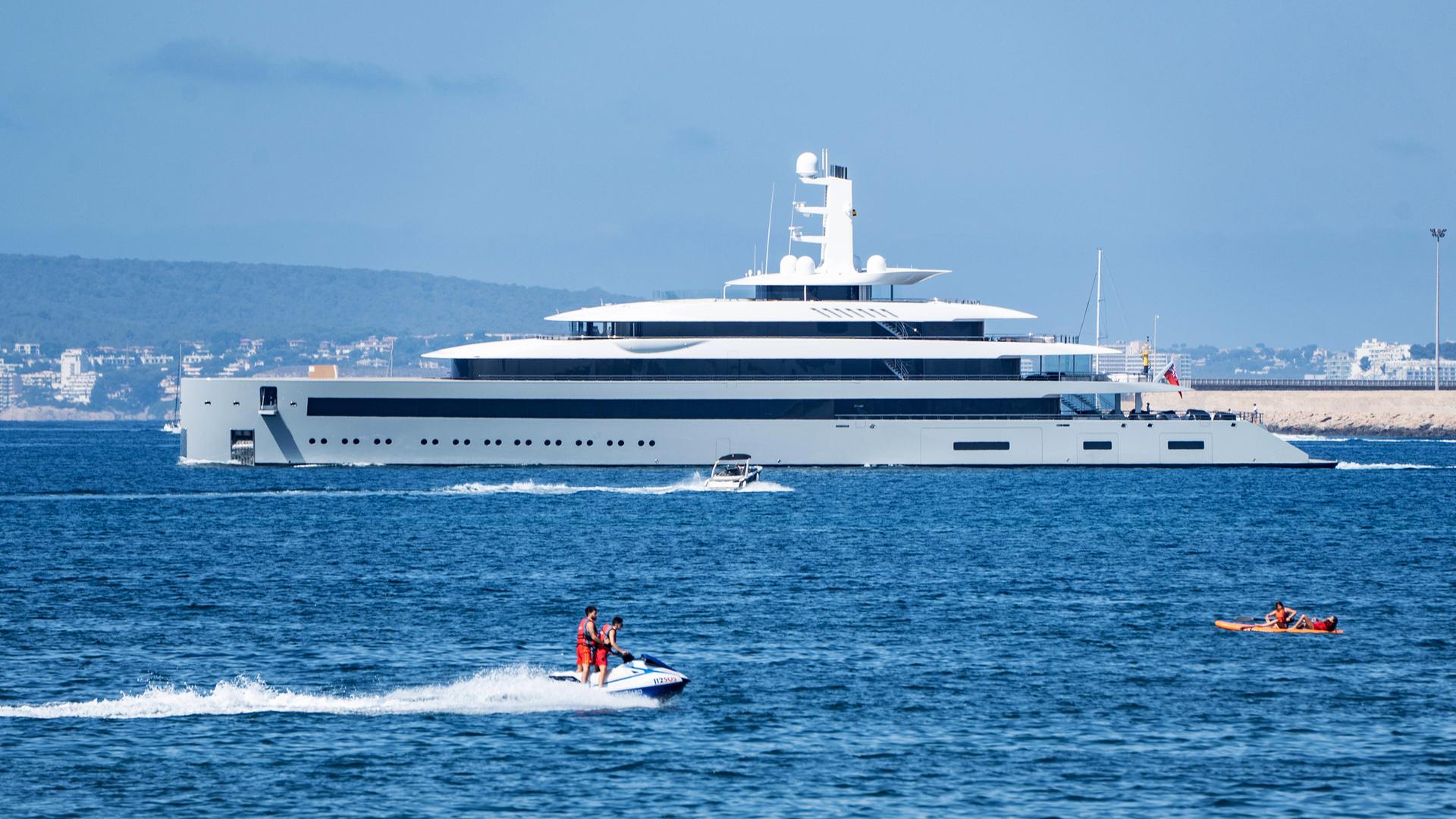 Eine Superjacht auf dem Meer, im Vordergrund sind kleine Boote mit Menschen zu sehen.