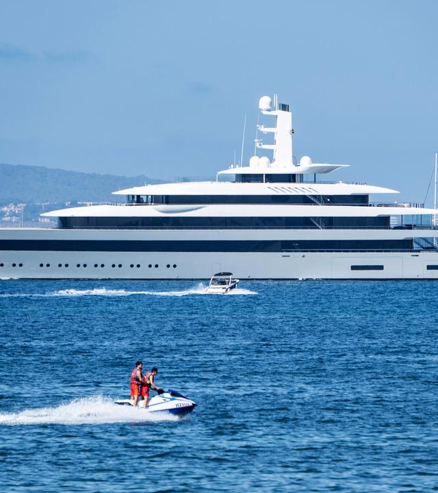 Eine Superjacht auf dem Meer, im Vordergrund sind kleine Boote mit Menschen zu sehen.