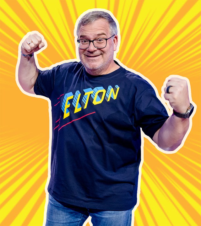 Moderator Elton steht im Mittelpunkt vor einem dynamischen, comicartigen Hintergrund mit gelben Strahlen. Er blickt lächelnd nach vorn, trägt ein T-Shirt mit der Aufschrift „ELTON“ und hält beide Fäuste erhoben, als würde er einen Erfolg feiern.