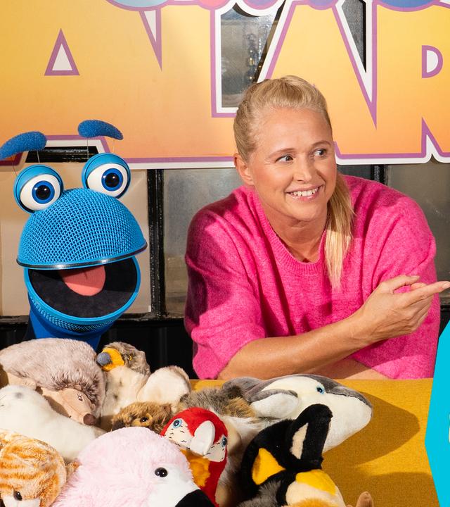Auf dem Bild sieht man SingDing, Singa und Senta (v.l.n.r.). SingDing und Singa lehnen sich über ein Sofa, auf dem sehr viele verschiedenen Stofftiere liegen. Singa zeigt nach rechts zu Senta, die stolz in die Kamera lächelt.