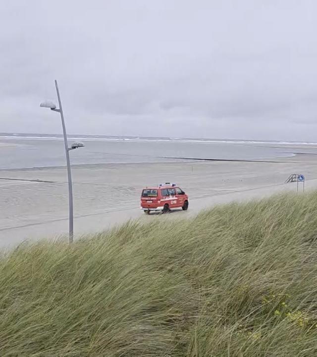 DLRG-Auto fährt am leeren Strand von Borkum bei einem Herbststurm.