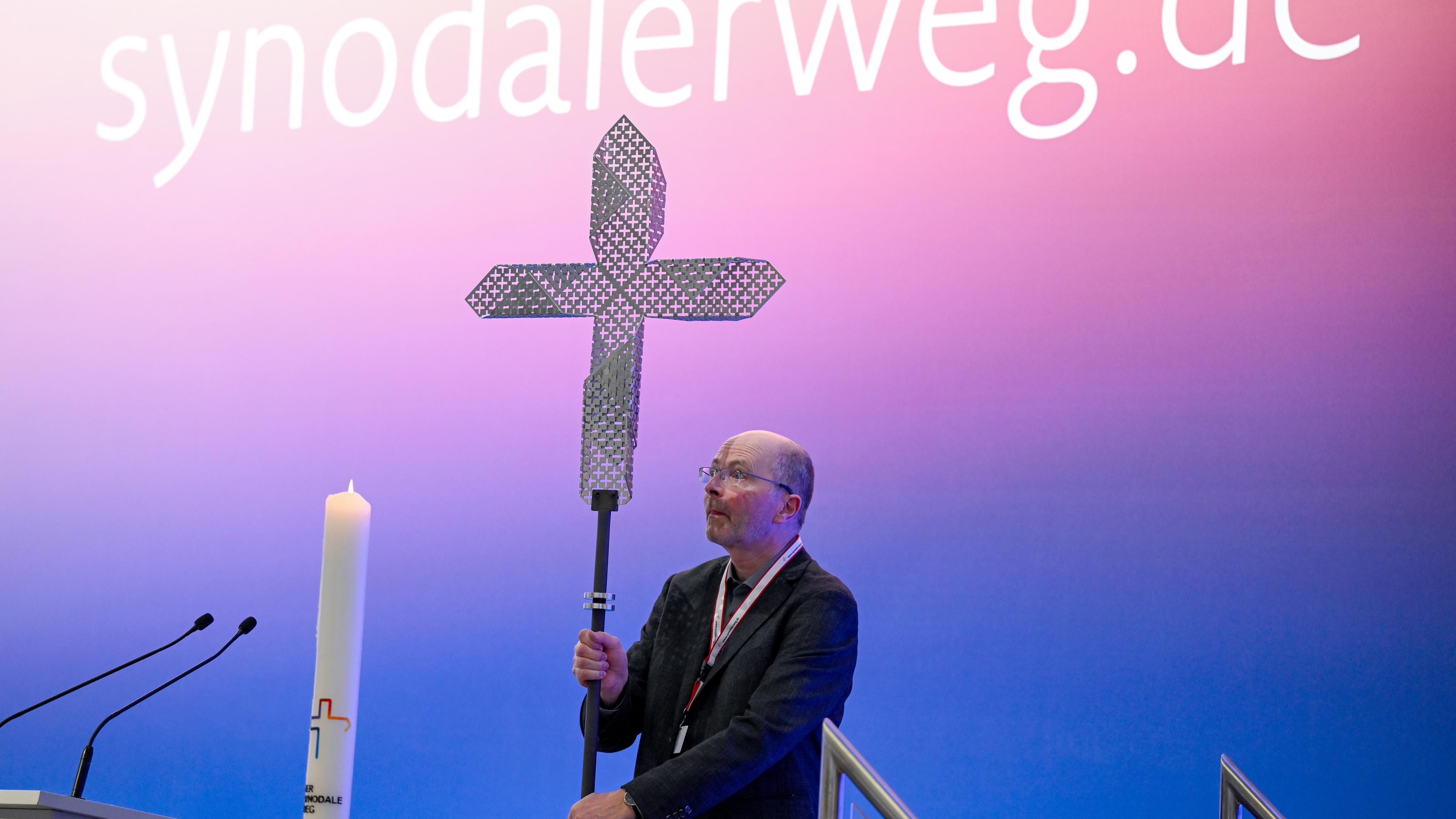 Hessen, Frankfurt/Main: Vor dem Schriftzug ·synodalerweg.de· wird auf der Synodalversammlung ein Kreuz auf dem Podium aufgestellt.