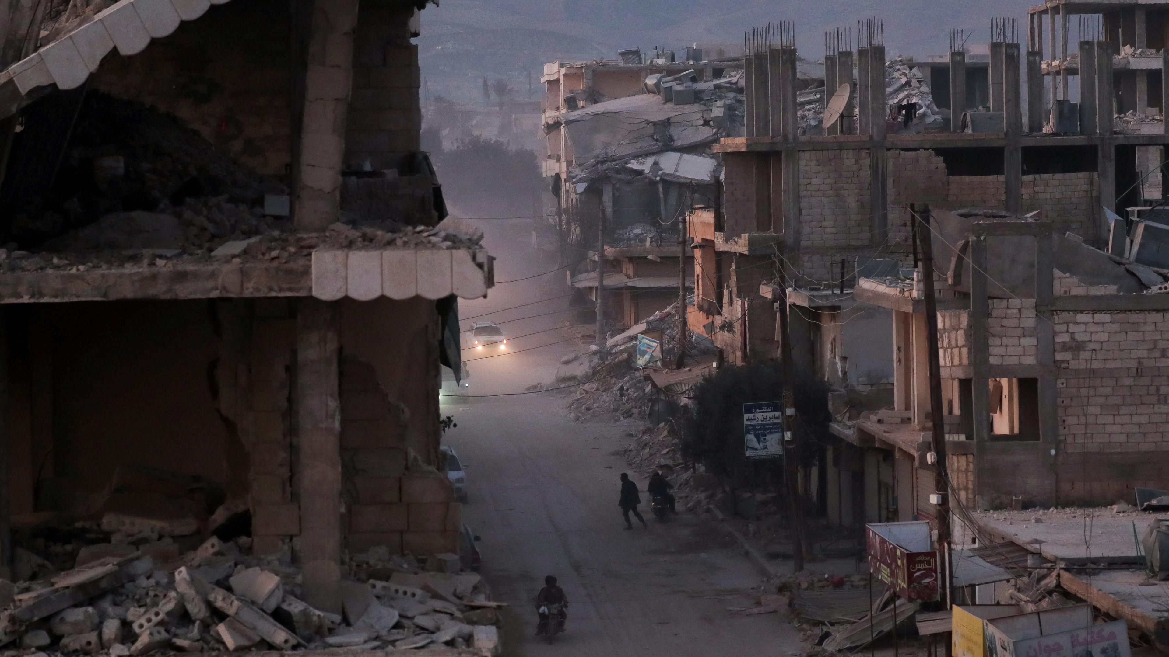 Menschen gehen nach einem Erdbeben in der Stadt Jandaris in Syrien an beschädigten Gebäuden vorbei.