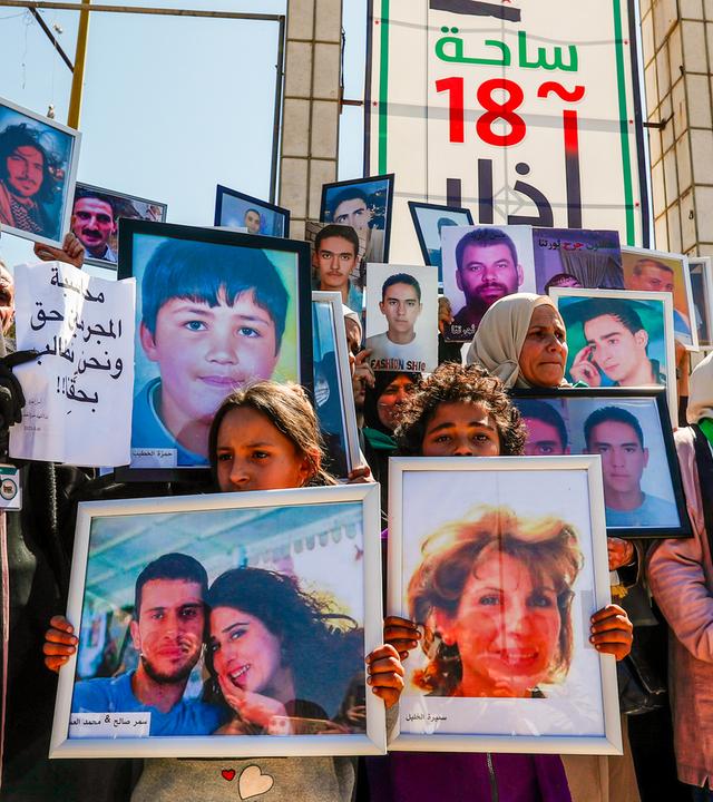 Frauen mit Kopftüchern und teils mit verhülltem Gesicht, sowie Kinder halten Fotos von vermissten Familienmitgliedern hoch.