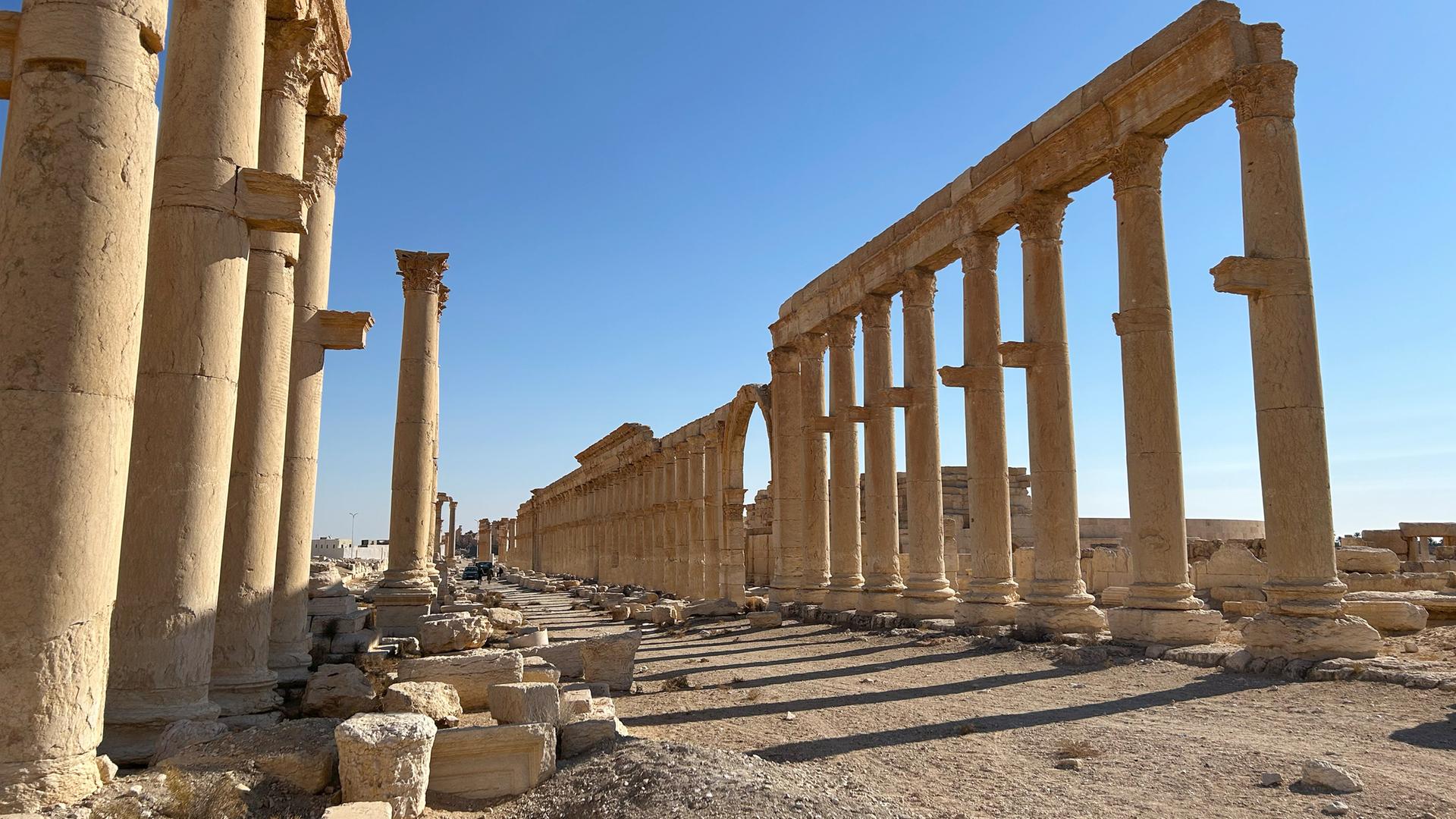 antike Säulen stehen vor blauem Himmel im Wüstensand.
