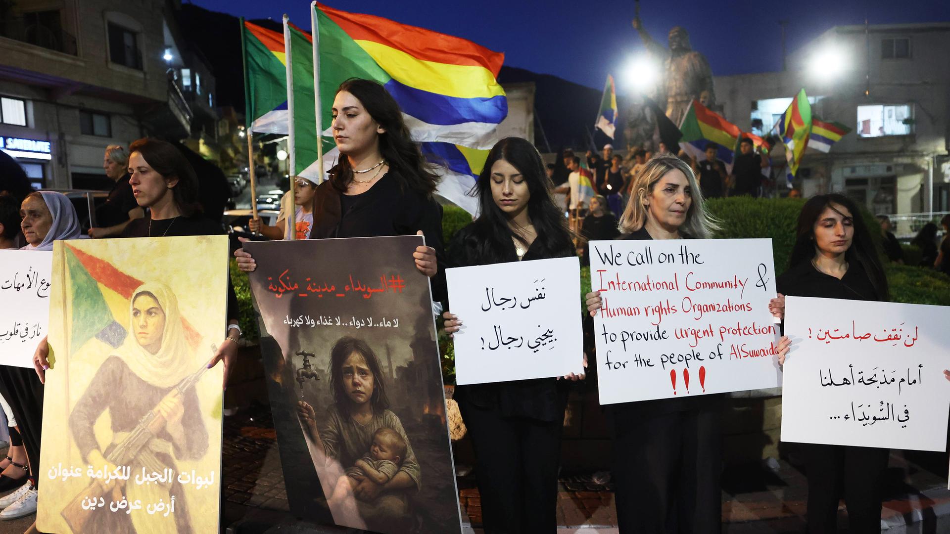 Mehrere Menschen halten Banner und Plakate bei einer Demonstration im Dunkeln.