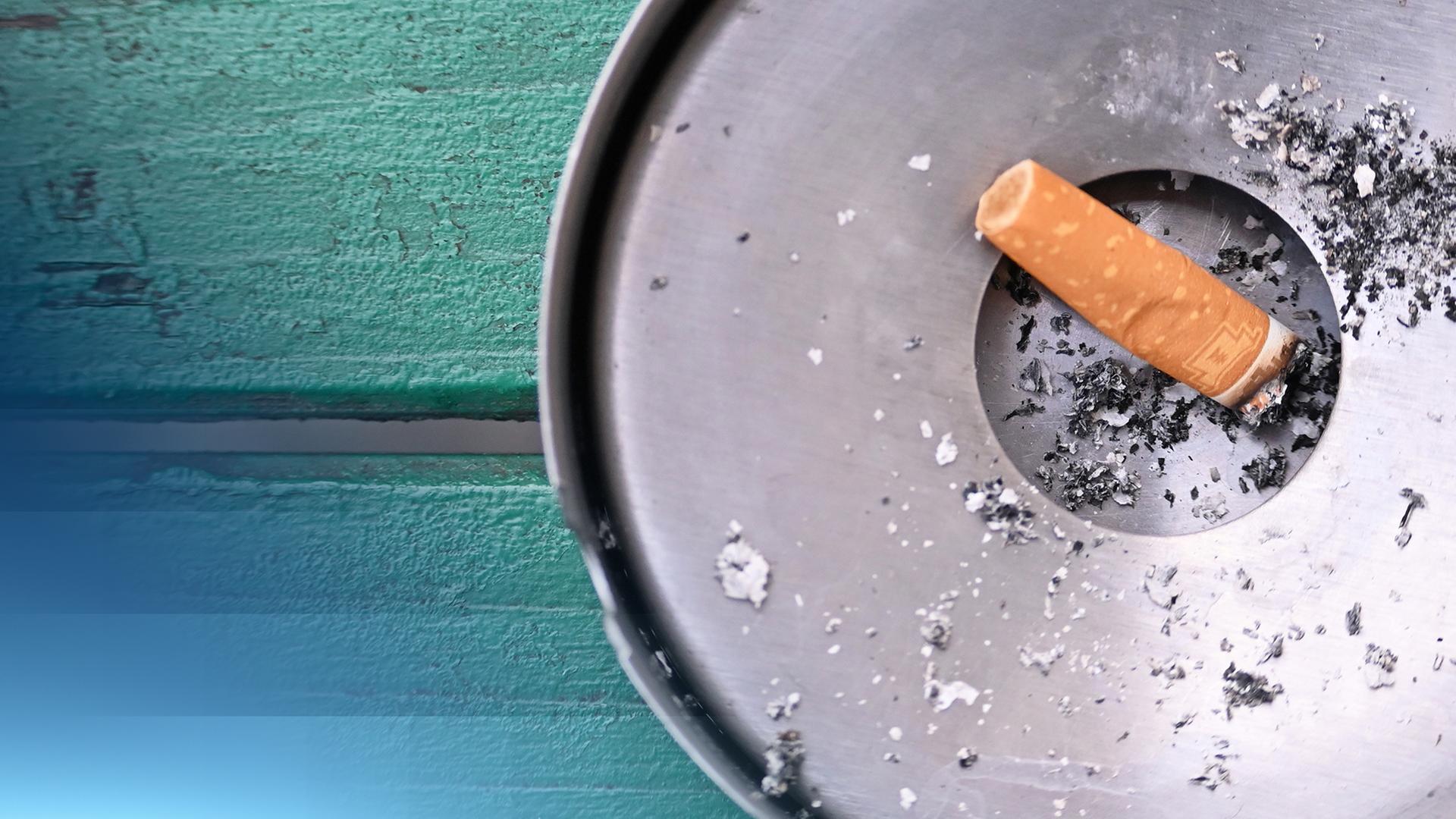 Kamerawinkel von oben: eine aufgerauchte Zigarette in einem metallenen Aschenbecher.