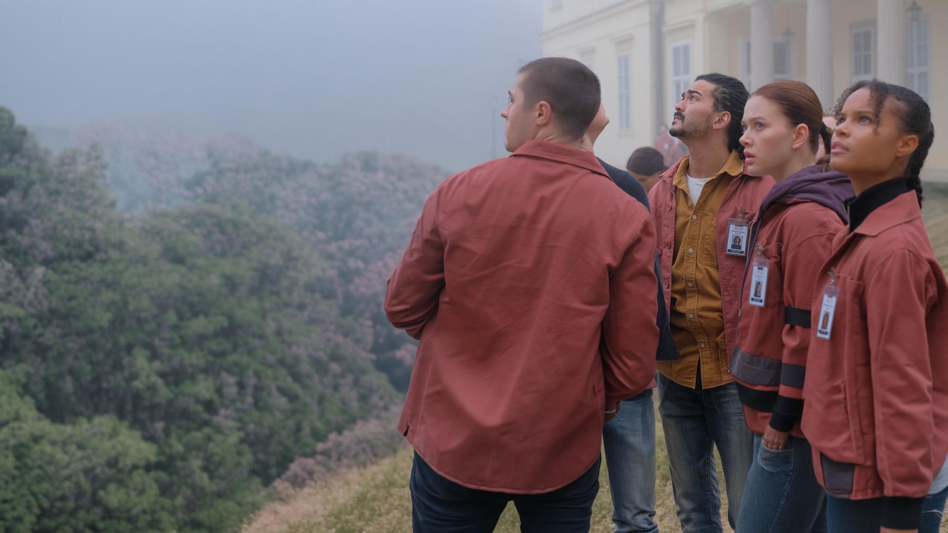 "Fallen - Schatten": Daniel (Gijs Blom), Roland (Lawrence Walker), Luce (Jessica Alexander) und Gabbe (Indeyarna Donaldson-Holness) blicken angespannt nach oben. Im Hintergrund ist ein helles Gebäude im dichten Nebel zu erkennen.