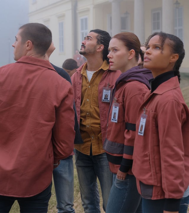 "Fallen - Schatten": Daniel (Gijs Blom), Roland (Lawrence Walker), Luce (Jessica Alexander) und Gabbe (Indeyarna Donaldson-Holness) blicken angespannt nach oben. Im Hintergrund ist ein helles Gebäude im dichten Nebel zu erkennen.