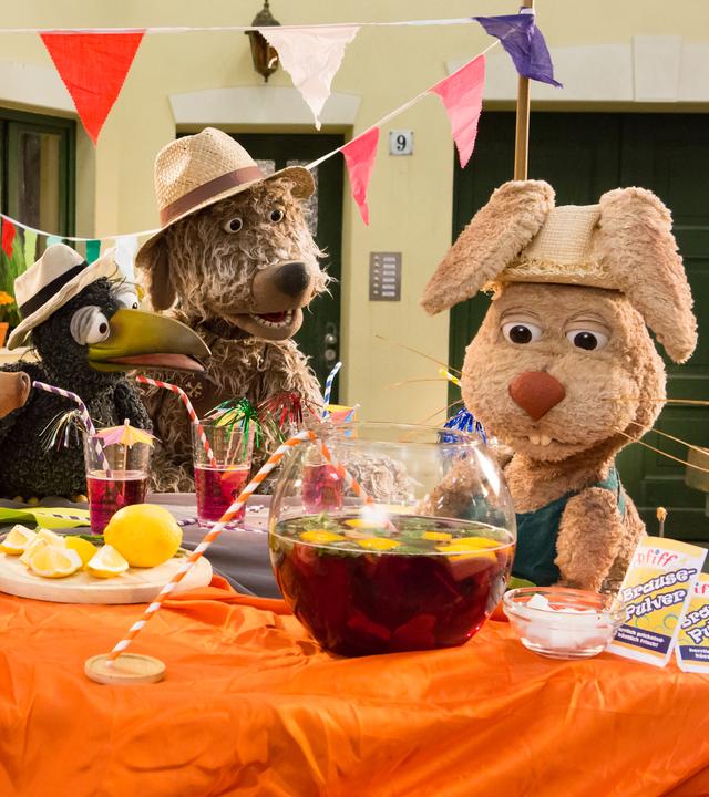 Die Freunde von Rudis Rasselbande stehen im Hof um einen Tisch versammelt. Alle schauen angespannt auf Otto, der wiederum ein mit Limonade gefülltes Bowleglas betrachtet.