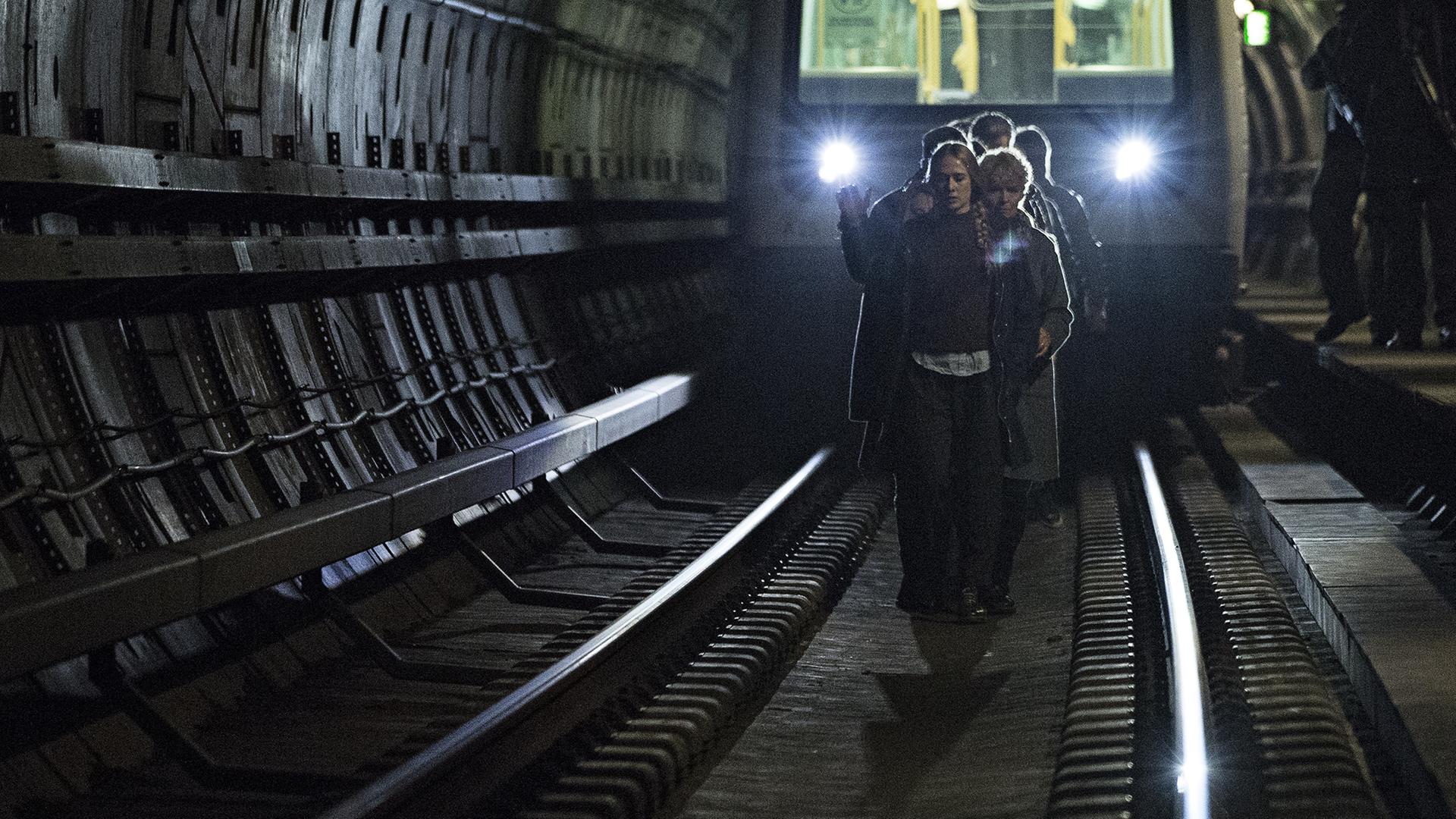 Bewaffnete Männer bewachen eine Gruppe von Menschen, die zu Fuß in einem U-Bahn-Tunnel laufen.