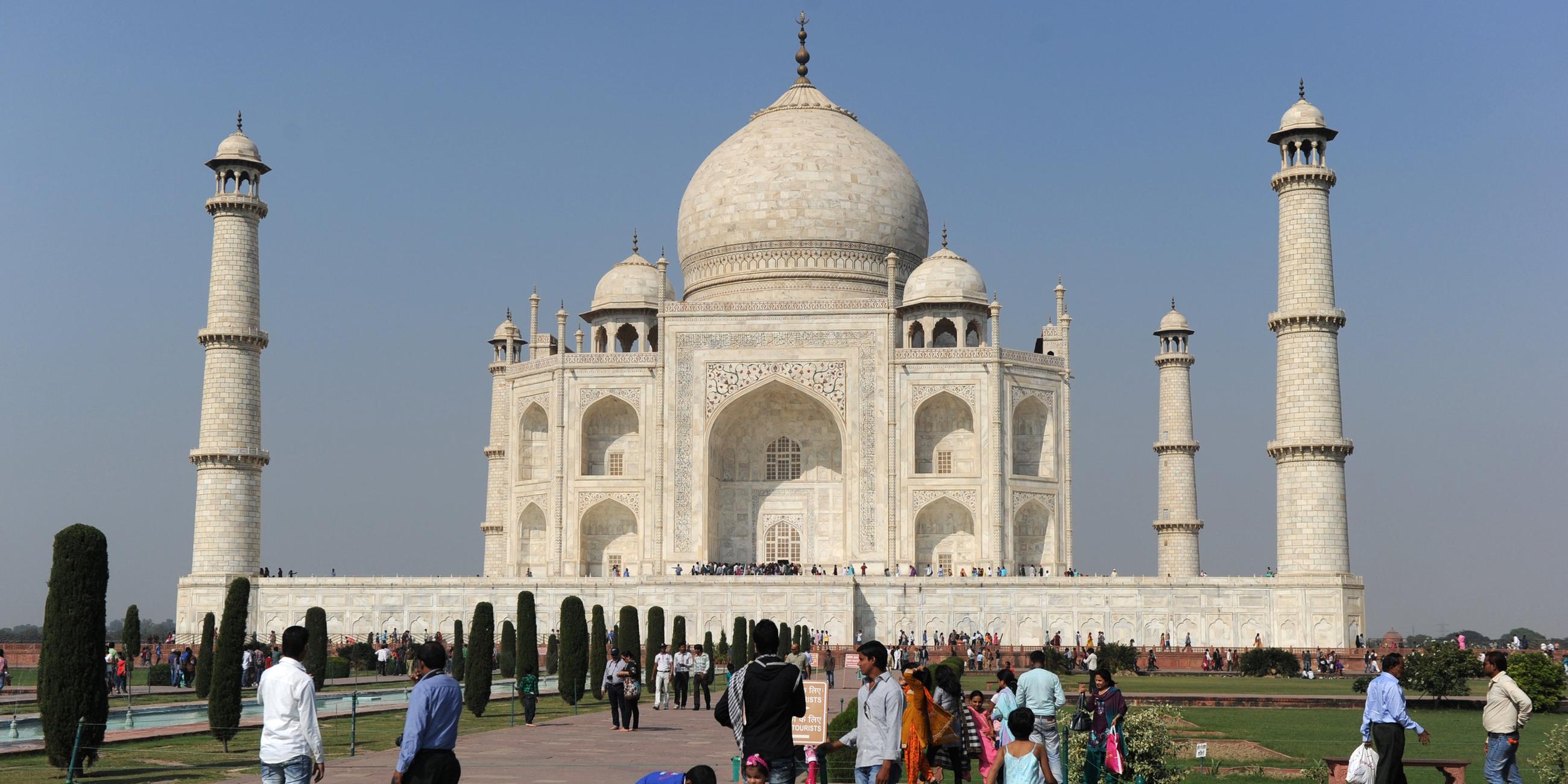 Das Taj Mahal steht vor wolkenfreiem Himmel. Menschen befinden sich auf dem Gelände.