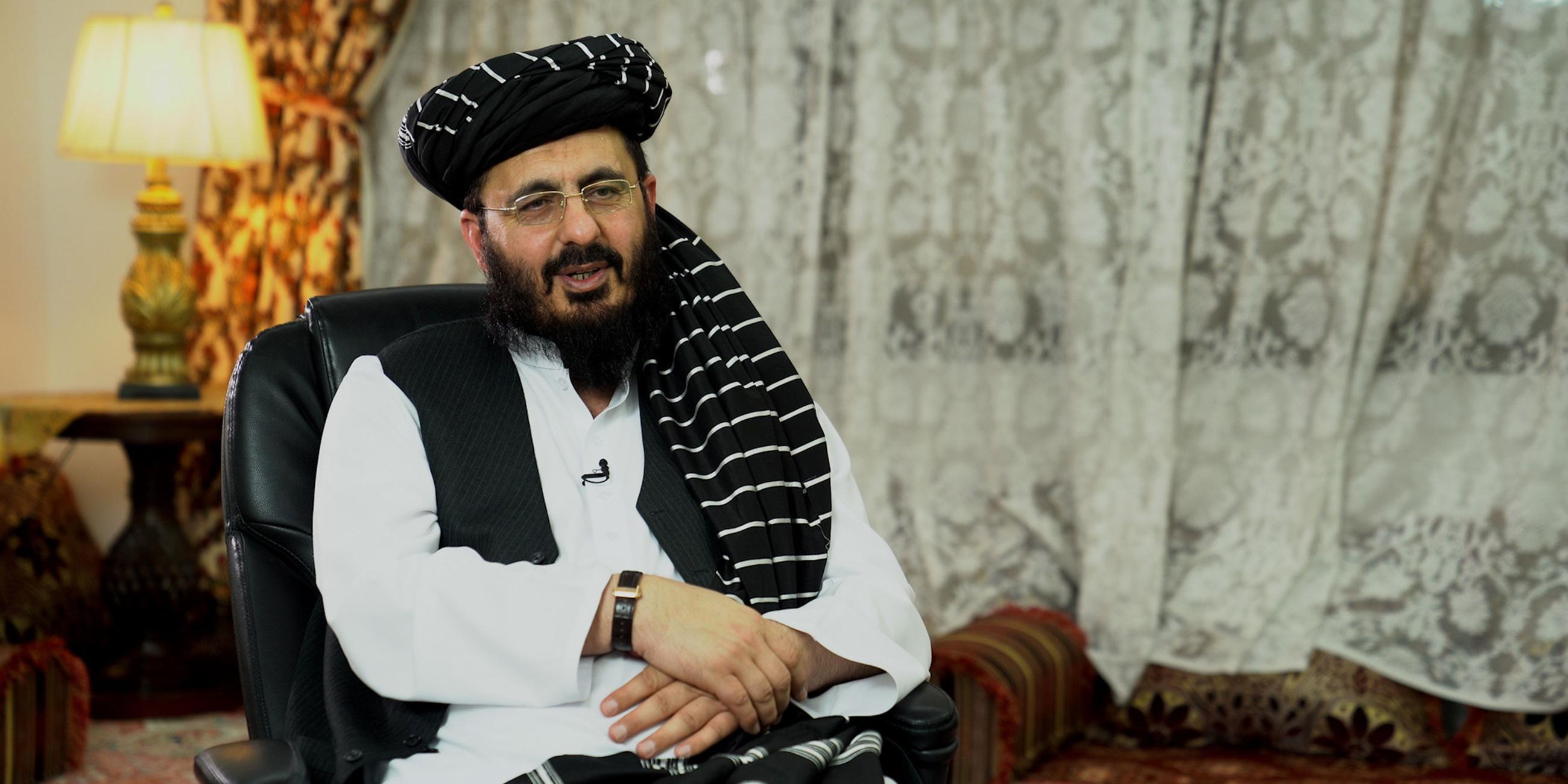 Mohammad Nabi Omari sitzt auf einem Sessel in einem Wohnzimmer. Er trägt weiße Kleidung, eine Brille, einen Bart und einen schwarzen Turban.