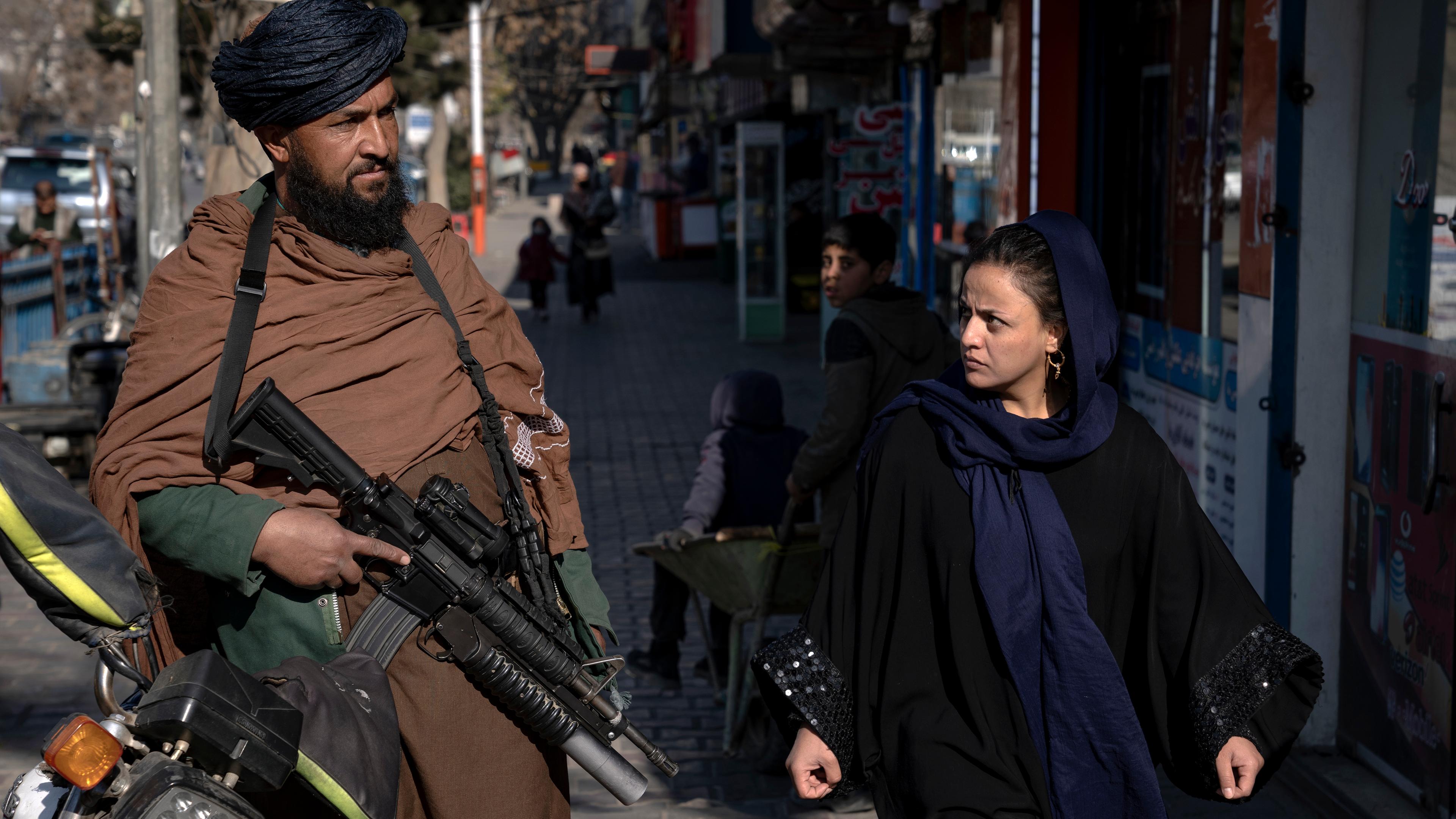 Ein Taliban-Kämpfer in Kabul steht Wache, während eine Frau vorbeiläuft. 