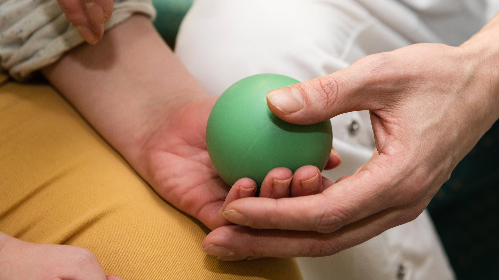 Pfleger legt Gummiball zum Ertasten und Fühlen in die Hände der Pflegebewohnerin.