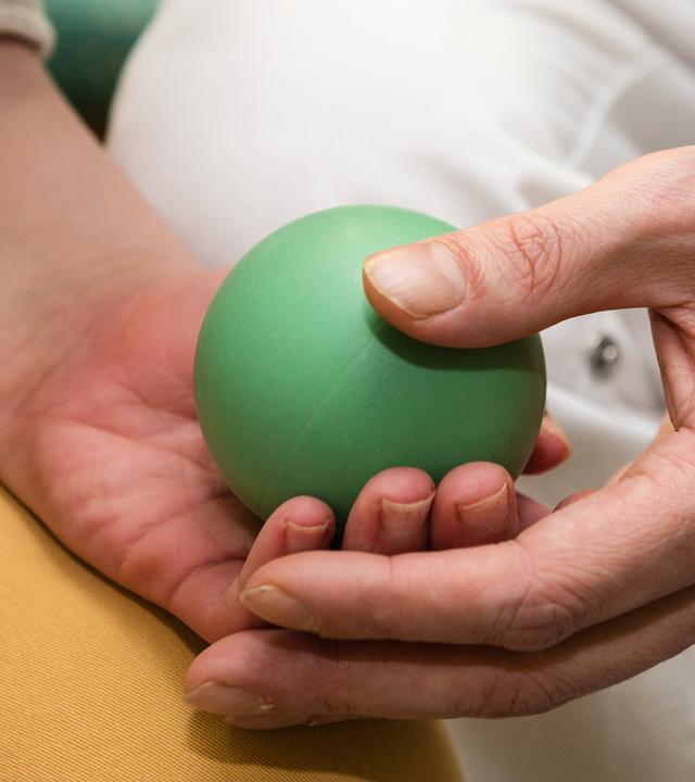 Pfleger legt Gummiball zum Ertasten und Fühlen in die Hände der Pflegebewohnerin.