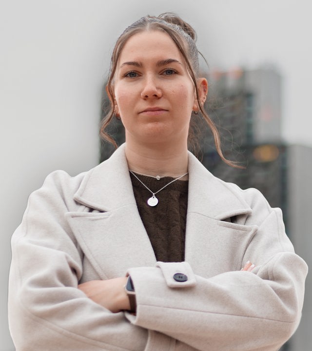 Eine junge Frau blickt ernst und traurig nach vorne. Im Vordergrund ist ein schwarzer Schatten zu sehen.