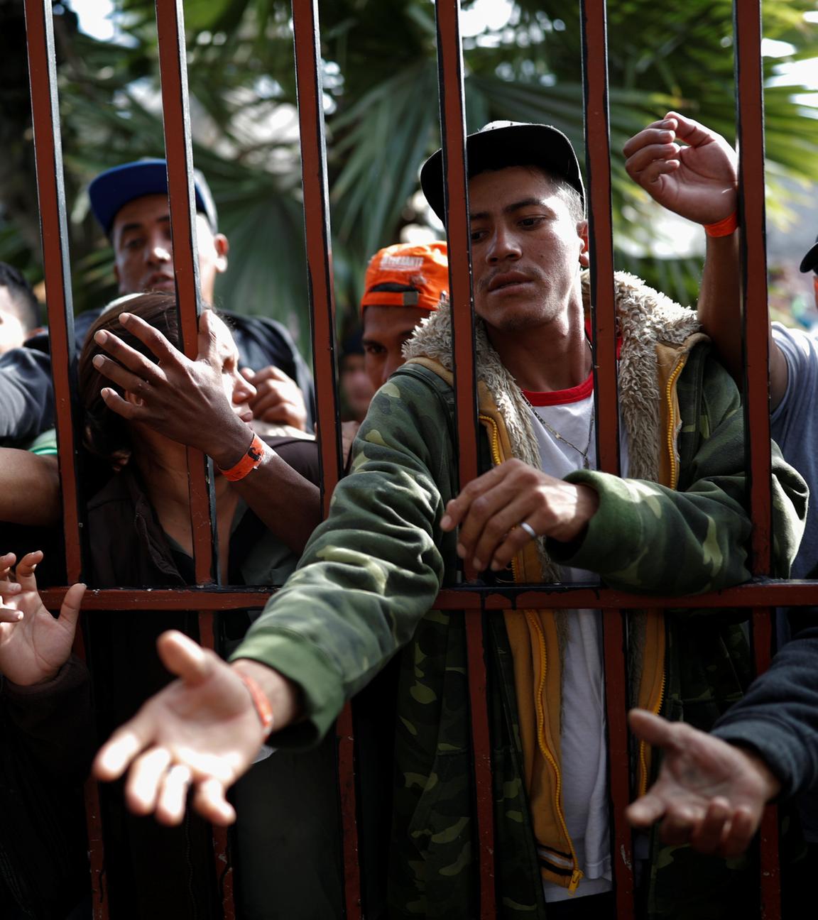 Migranten aus Mittelamerika stehen an einem Tor und stecken ihre Hände und Arme hindurch am 18.11.2018 in Tijuana.