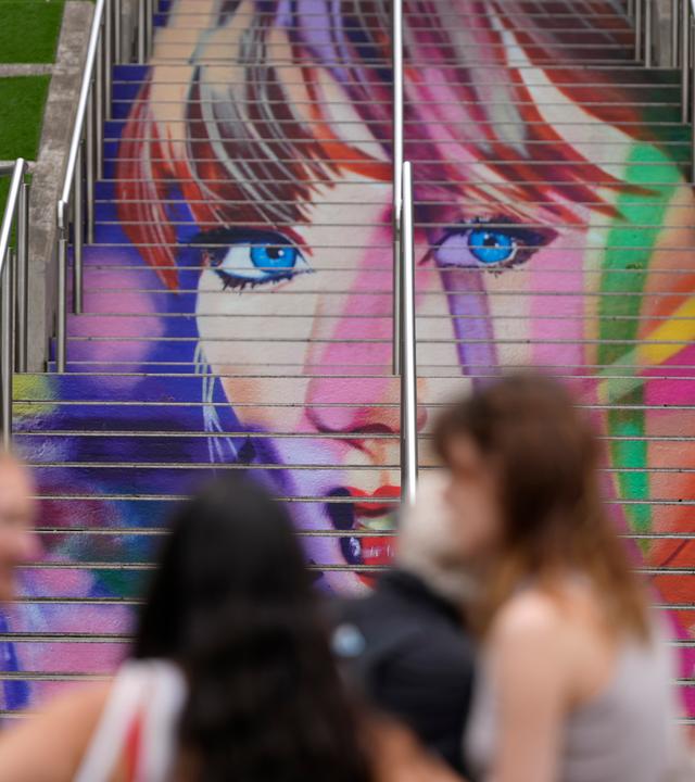 Fans posieren am Mittwoch, den 14. August 2024, vor einem Porträt von Taylor Swift, das auf einer Treppe im Wembley-Stadion in London gemalt ist, im Vorfeld einer Reihe von Taylor Swift-Konzerten, die am Donnerstag beginnen. 