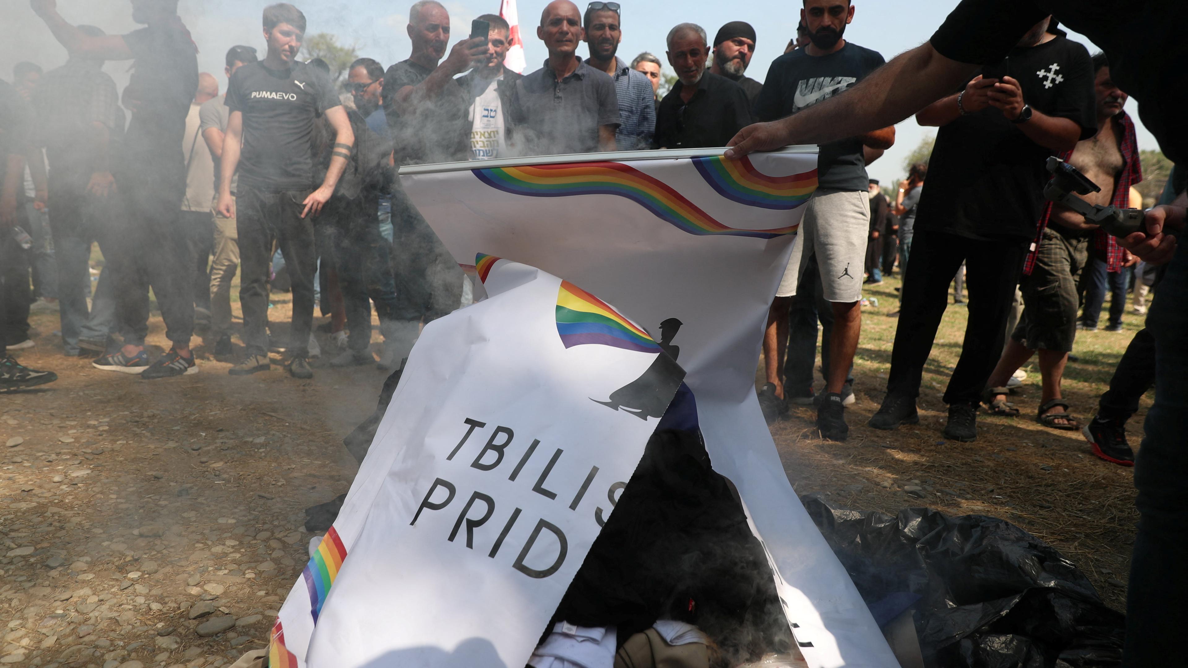 Gegner des Pride Festes verbrennen ein Regenbogen-Plakat. 