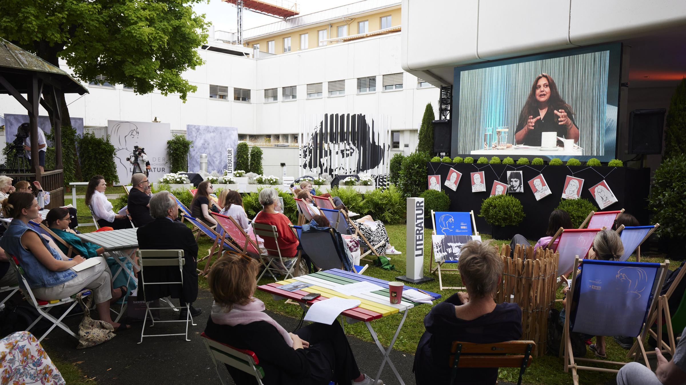 Publikum mit Liegestühlen auf einer Wiese in Blickrichtung zu einem großen Monitor aufgestellt