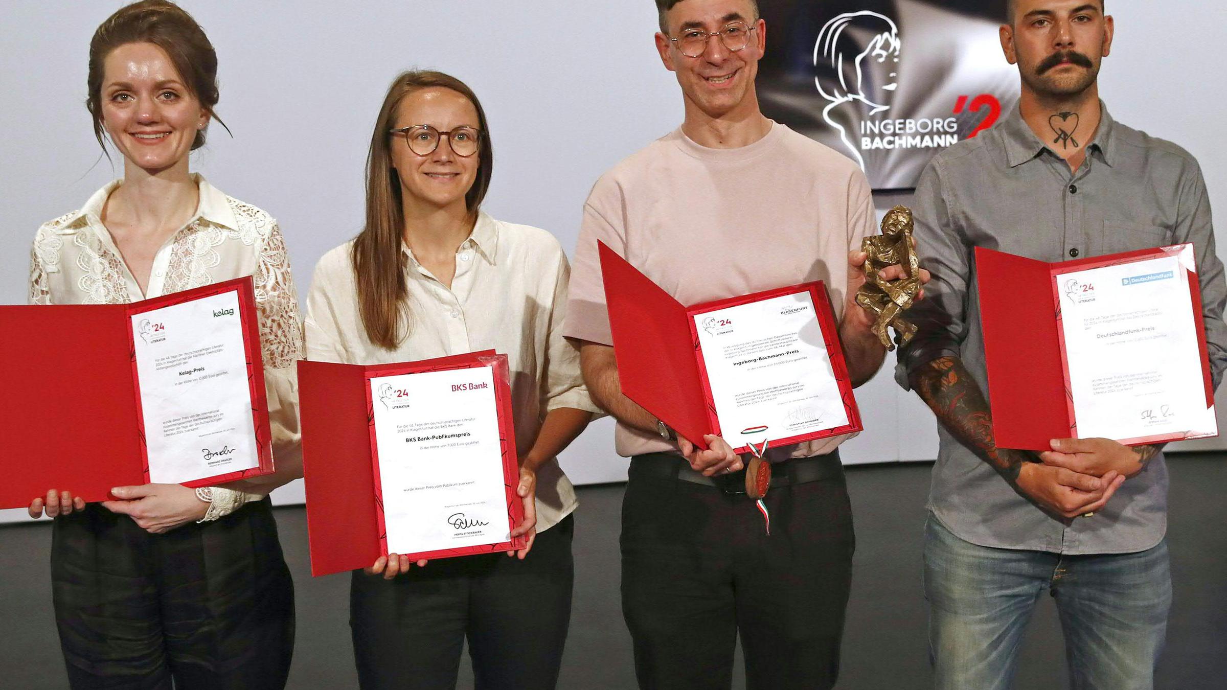 Zwei Frauen und zwei Männer stehen in einer Reihe und halten Mappen mit Preiszertifikaten vor sich.