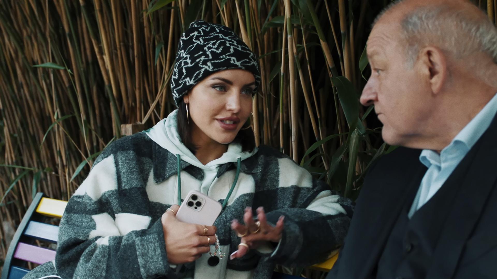 Bonnie (Johanna Ingelfinger), eine stylische junge Frau, sitzt mit Wilsberg (Leonard Lansink) auf einer Parkbank. Bambusstauden im Hintergrund.
