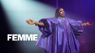 Femme": Halbnahe: Jules (Nathan Stewart-Jarrett) steht als Dragqueen in einem opulentem lila Kleid mit dünn geflochtenen Zöpfen und ausgebreiteten Armen in Scheinwerferlicht auf Bühne. 