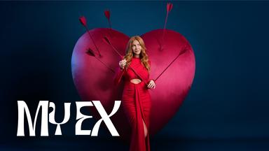 Ivy (Palina Rojinski) steht in einem langen roten Kleid vor einem großen roten Samtherz in dem einige Pfeile stecken. Sie hält einen Pfeil in ihren Händen.