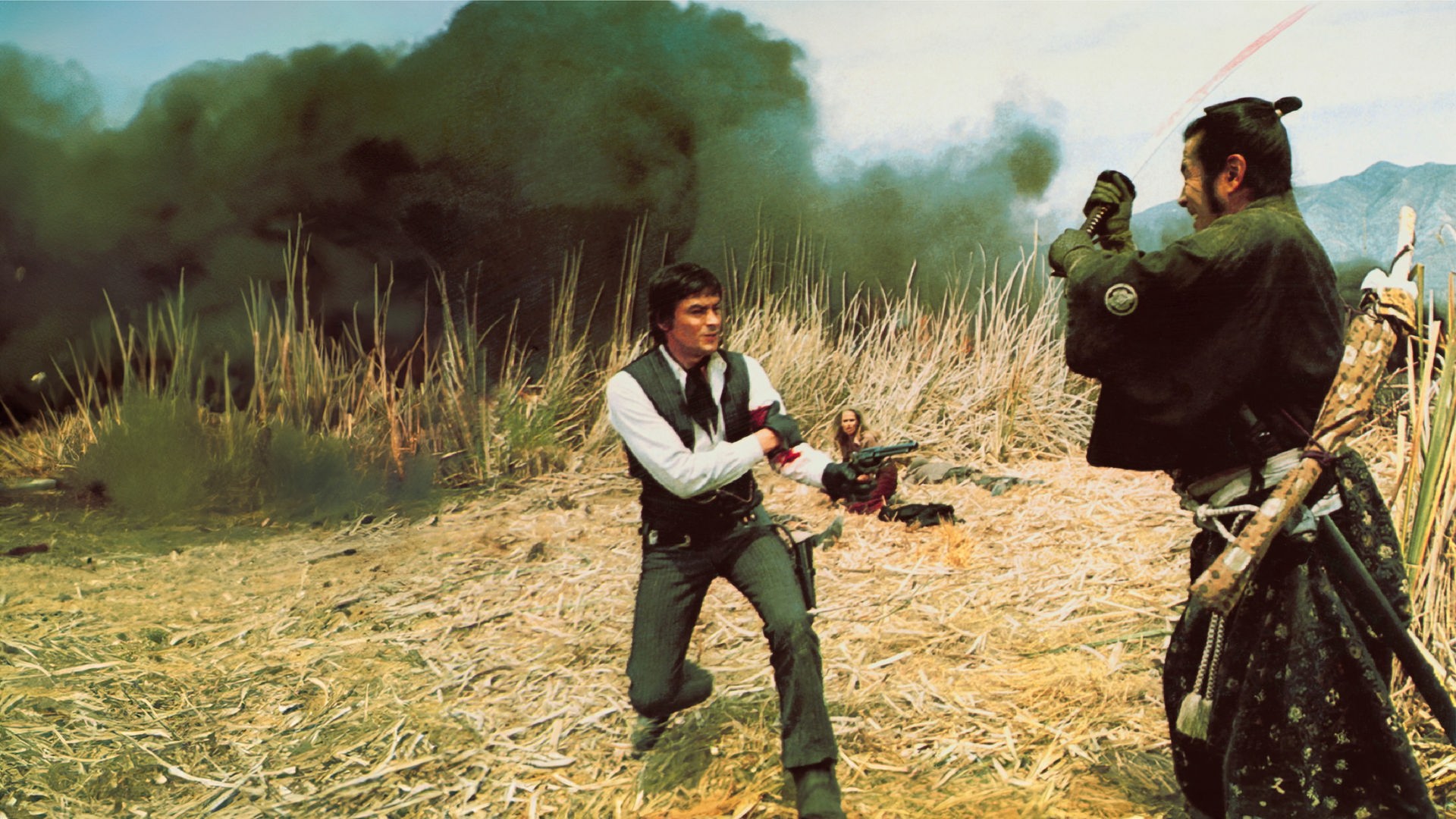 Gauche (Alain Delon) steht mit blutverschmiertem Arm und gezogener Pistole in einem Feld aus trockenem Gras, während Kuroda (Toshirô Mifune) ihm mit erhobenem Schwert gegenübersteht. Im Hintergrund sitzt Christina (Ursula Andress) geduckt zwischen den Gräsern, während dunkler Rauch aufsteigt.