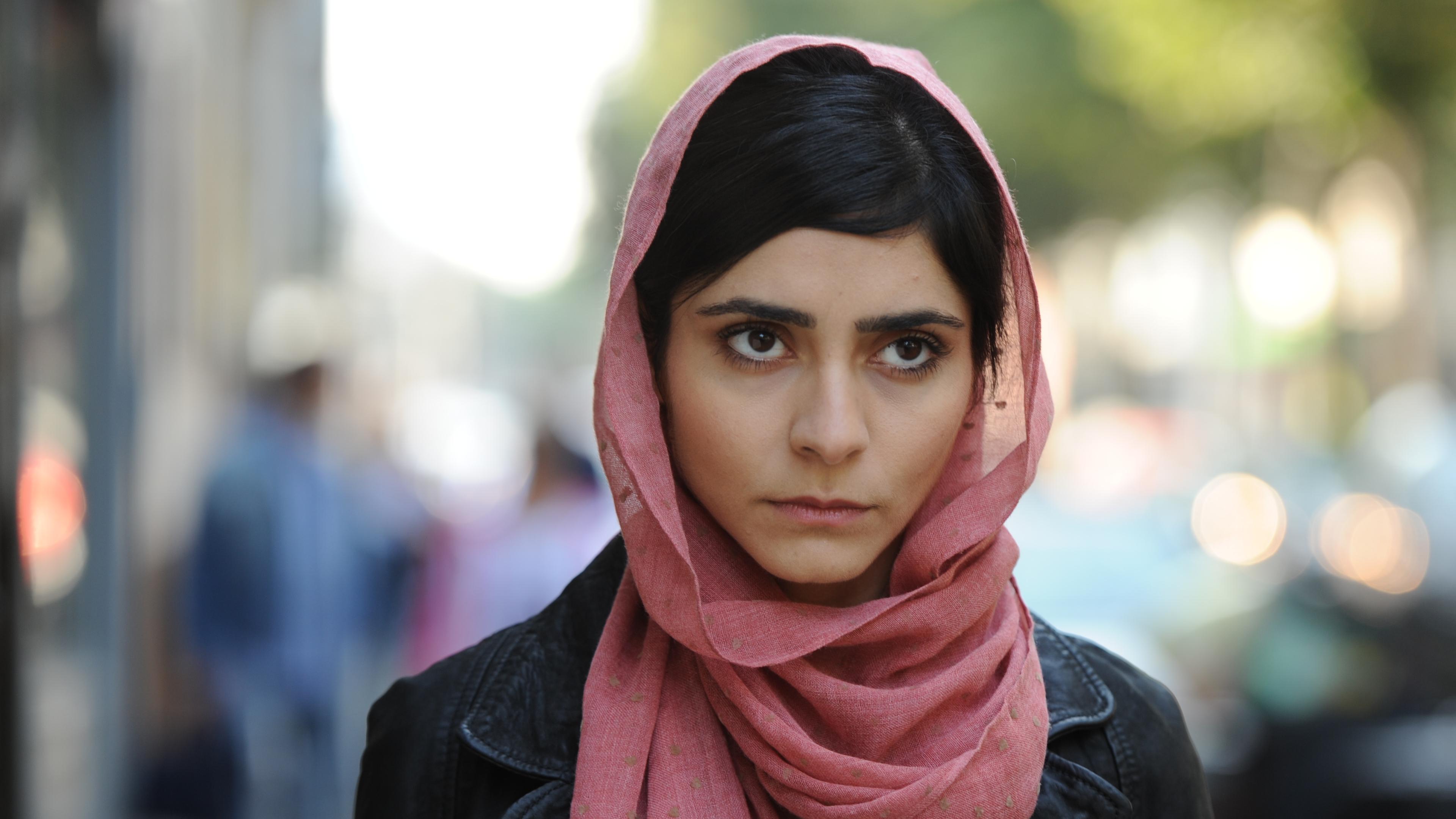 Lela, die einen Hidschab trägt, und Marc stehen vor einer Gruppe muslimischer Frauen. Im Hintergrund sind eine Tafel und eine in deutscher Tracht gekleidete Schaufensterpuppe zu sehen.